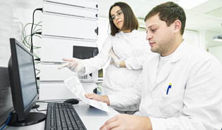 Man and woman wearing lab coats and looking at computer
