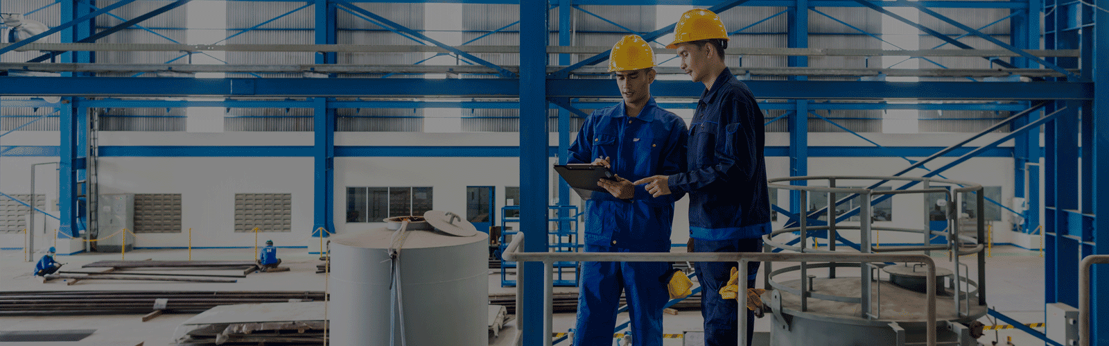 Two men in a factory wearing yellow hard hats. 